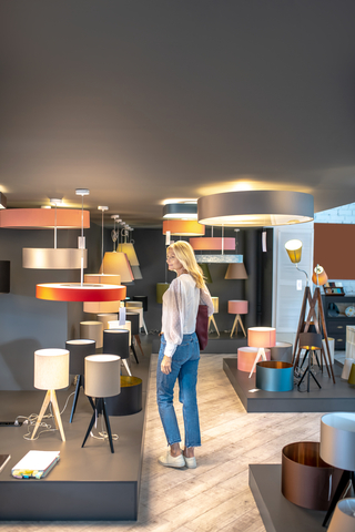 Assortment of fixtures. Woman in jeans and white sneakers walking through the exhibition hall where the lamps are presented, an interested looking.